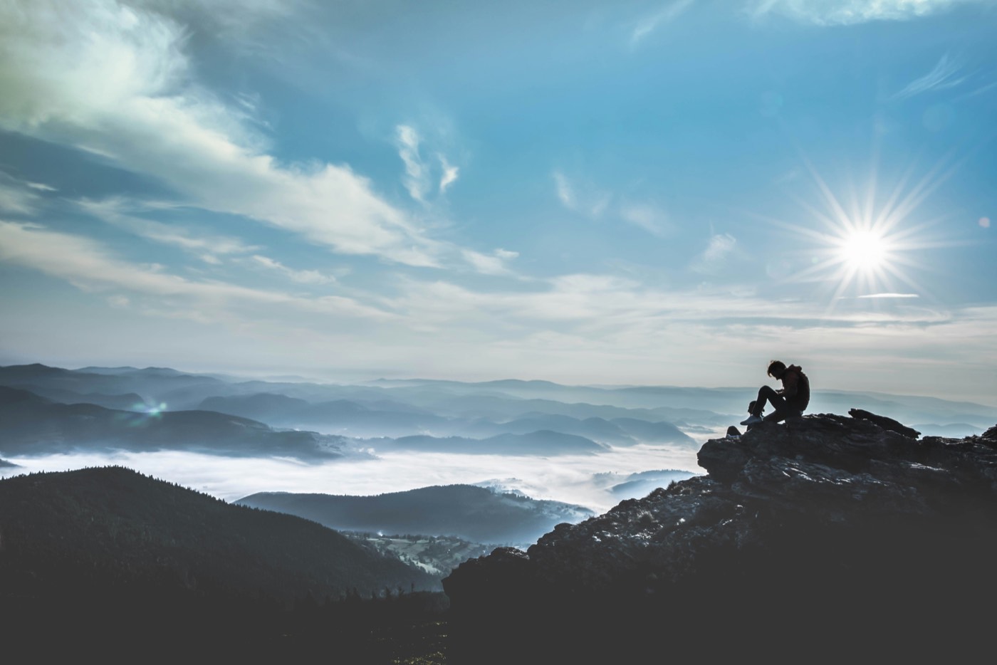 Person sitzt auf einem Berggipfel über dem Nebelmeer